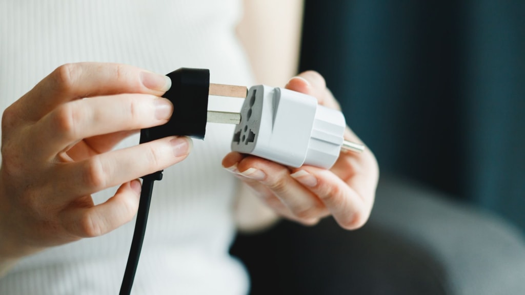 Person holding and connecting a black electrical plug to a white travel adapter—essential for your Costa Rica packing list to ensure your devices stay charged while exploring.